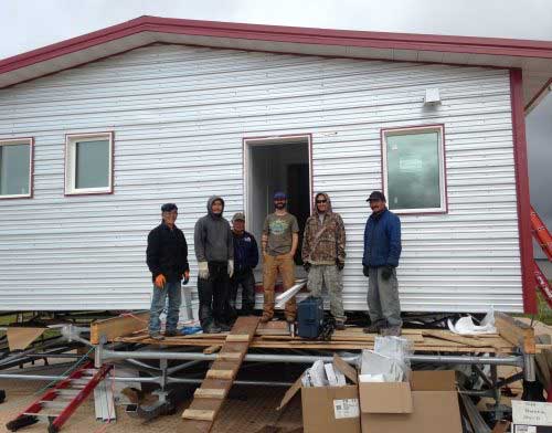 jpg Aaron Cooke, in the T-shirt and blue hat, poses in front of an efficient house he helped design after he and Newtok residents built it at the new village site of Mertarvik in 2016.
