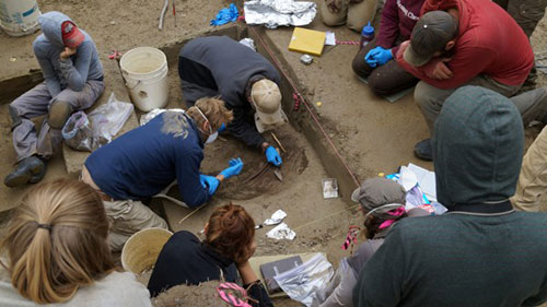 jpg Members of the archaeology field team watch as University of Alaska Fairbanks professors Ben Potter and Josh Reuther excavate the burial pit at the Upward Sun River site.