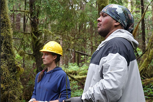 jpg Kelsey Dean, watershed scientist with the Southeast Alaska Watershed Coalition, and Kaagwaan Eesh Manuel Rose-Bell of Keex’ Kwáan watch as crew members set up tools to drag a log into place.